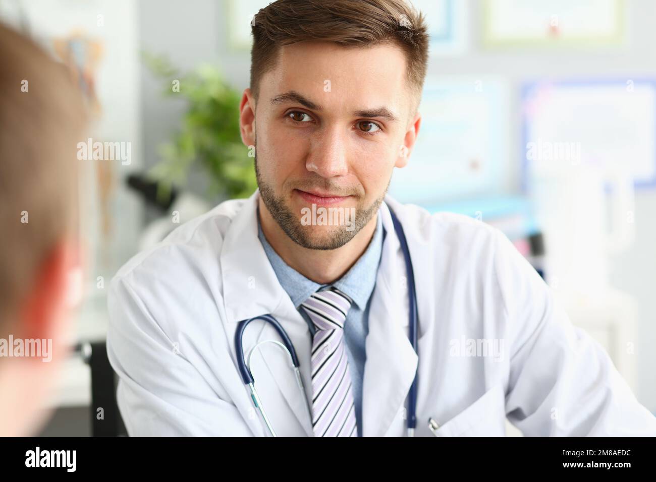 Der junge Arzt berät und hört dem Patienten in der Klinik zu Stockfoto