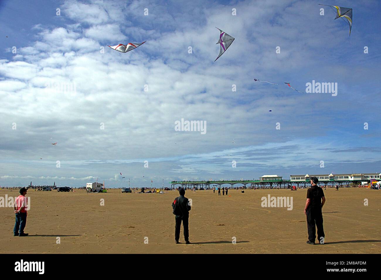 Beim St. Annes Kite Festival stehen drei Menschen unter drei Drachen. Stockfoto