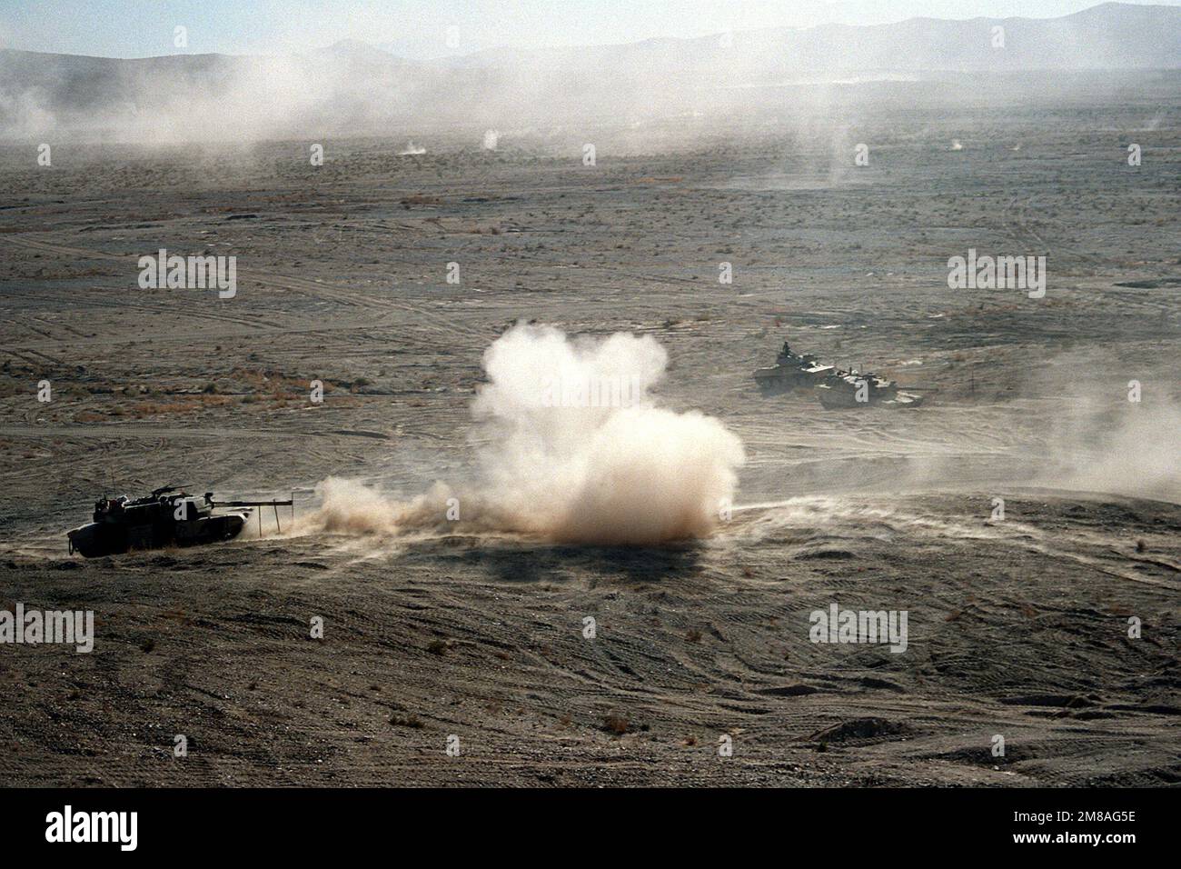 Eine Staub- und Rauchwolke rollt von einem M-1A1 Abrams Hauptwaffenpanzer der 24. Infanteriedivision (mechanisiert) weg, der während einer Feuerübung im National Training Center eine Kugel abgefeuert hat. Ein zweiter M-1 und ein M-551 Sheridan-Leuchtstofftank sind im Hintergrund rechts. Basis: Fort Irwin Bundesstaat: Kalifornien (CA) Land: Vereinigte Staaten von Amerika (USA) Stockfoto