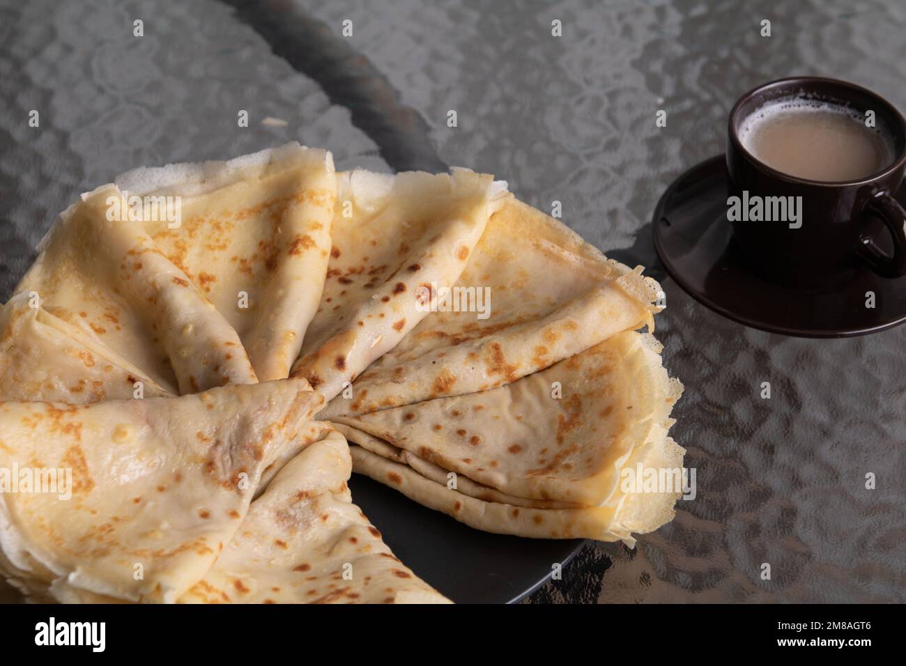 Machen Sie Fotos von dreieckigen gebratenen Pfannkuchen, die in einem Kreis auf einem Teller gestapelt sind, und einer dunklen Tasse Kaffee auf einem Glastisch Stockfoto