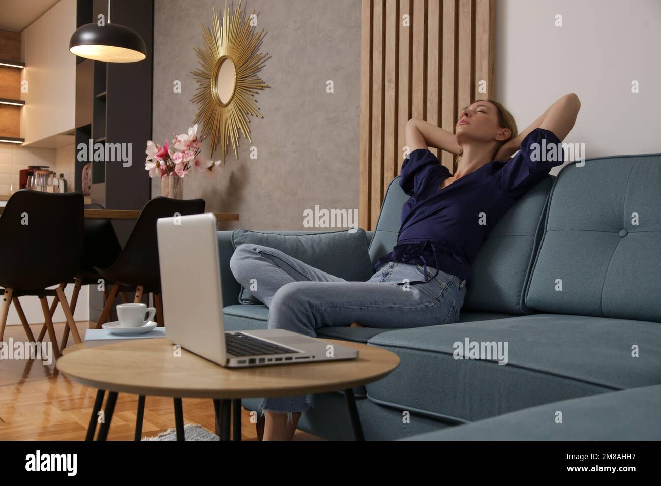 Junge Frau genießt einen gemütlichen, entspannten Nachmittag im Wohnzimmer vor dem Laptop, Freiberufler oder Unternehmerin, die eine Pause von der Arbeit macht. Stockfoto