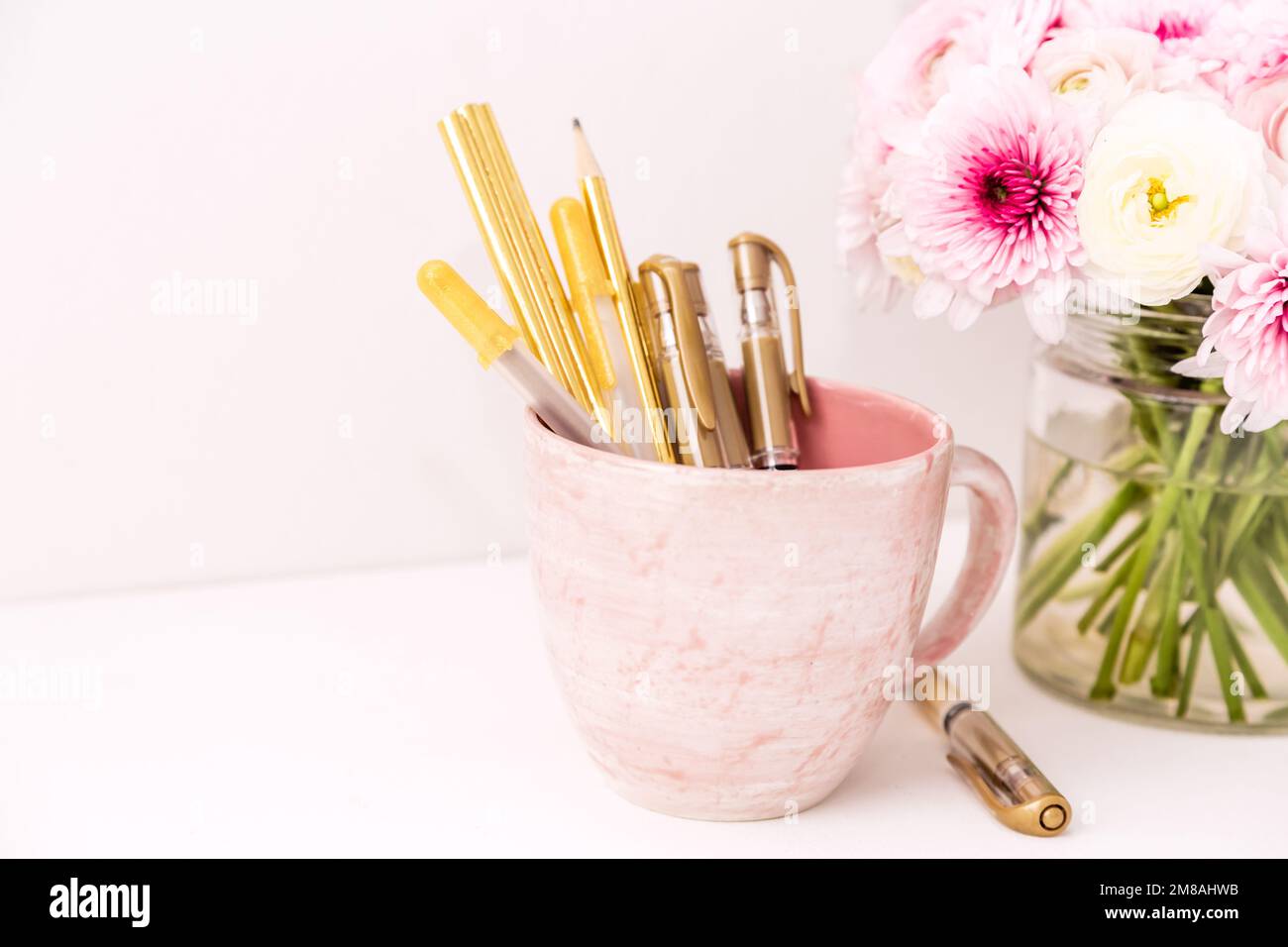 Femininer Schreibtisch mit goldenen und pinkfarbenen Schreibwaren, einschließlich frischer Blumen Stockfoto