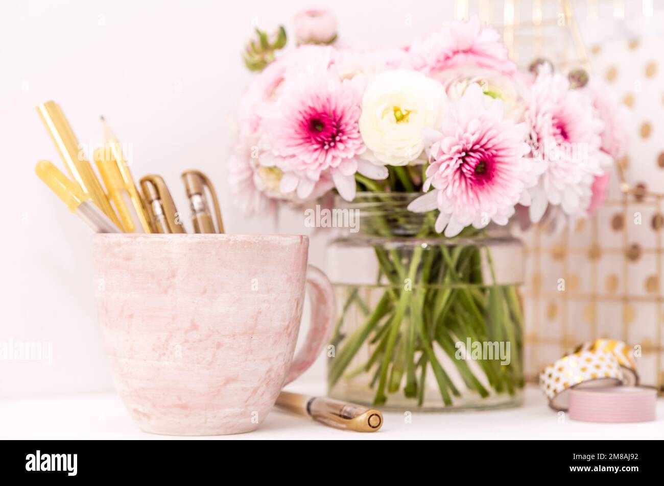 Femininer Schreibtisch mit goldenen und pinkfarbenen Schreibwaren, einschließlich frischer Blumen Stockfoto