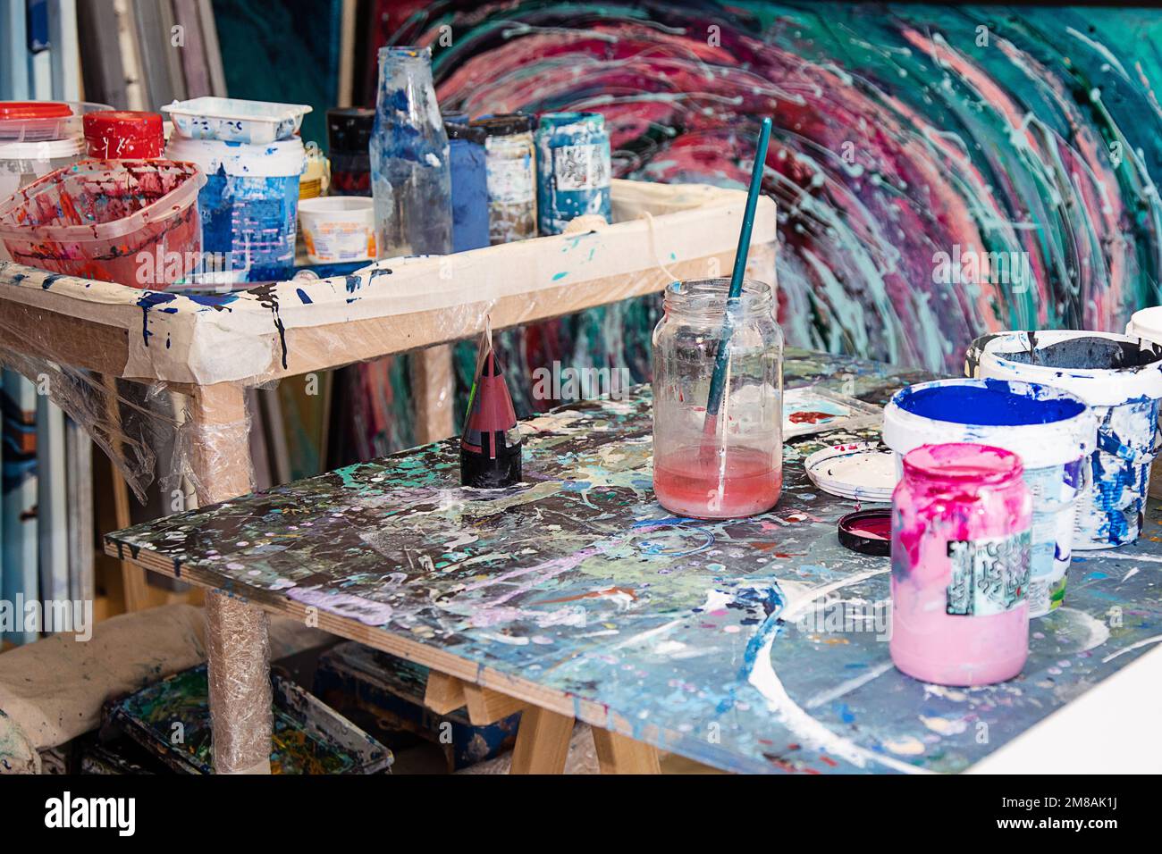 Interieur des Workshops für kreative Kunst. Verschiedene Eimer mit Farbe, schmutzige Glasgefäße, Holzschreibtische mit Farbe befleckt. Stockfoto