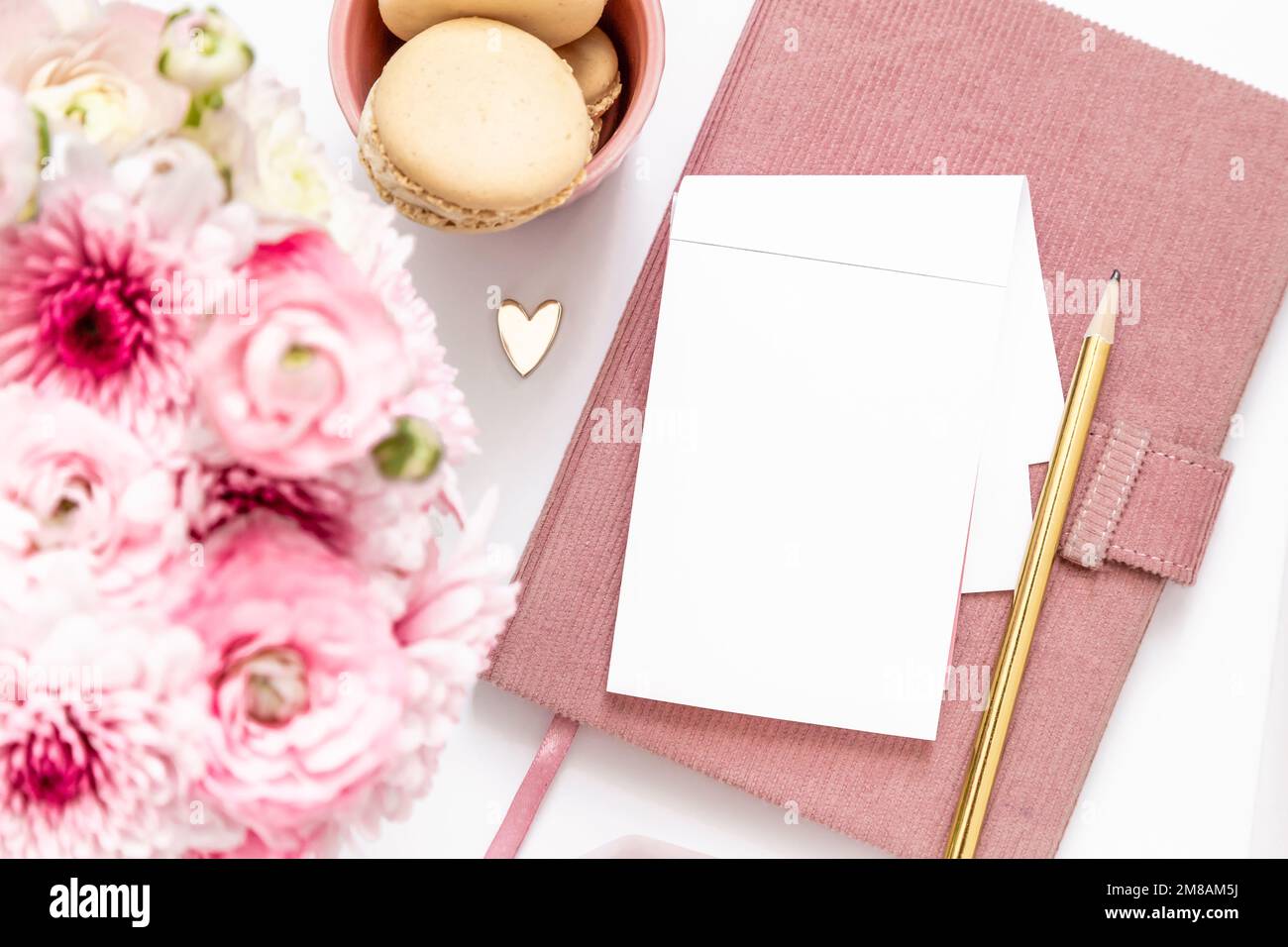 Feminine Gold- und Pink-Elemente wie Schreibwaren, Ohrstöpsel, Herz und Makronen Stockfoto