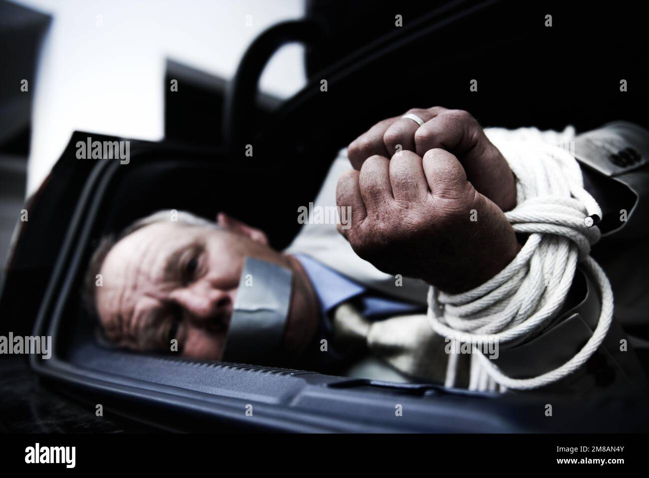 Es gibt kein Entkommen. Ein ängstlicher Geschäftsmann, gefesselt und geknebelt im Kofferraum seines Autos. Stockfoto