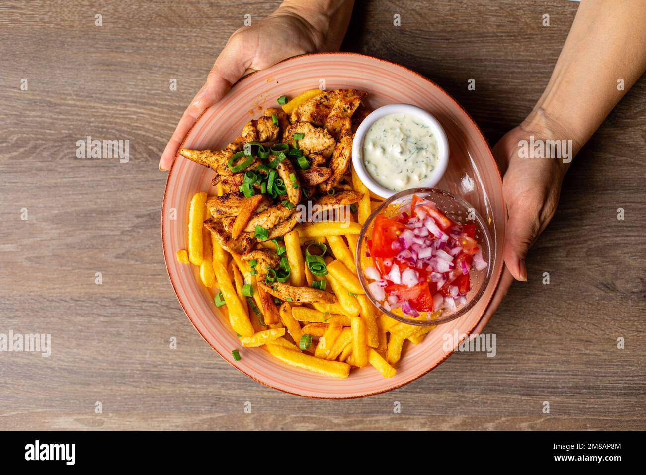 Draufsicht einer unbekannten Frau mit Pommes Frites, gebratenem Hähnchen, geschnittener Tomate mit roten Zwiebeln und weißer Sauce. Stockfoto