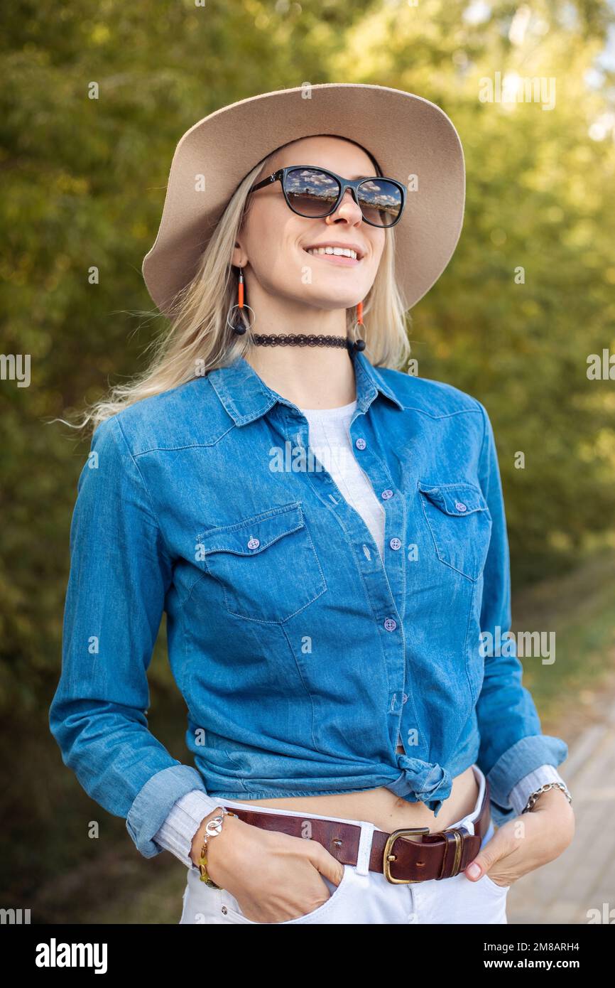 Vertikale, moderne, fröhlich lächelnde, blonde Frau mit Sonnenbrille und einem fröhlichen Urlaubsabenteuer in der Natur. Auf Reisen Stockfoto