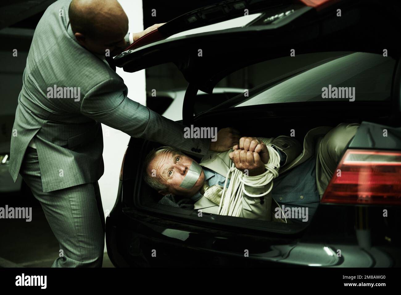 Gefesselt und geknebelt im Kofferraum. Ein Gangster stopft einen gefesselten und geknebelten Geschäftsmann in den Kofferraum seines Autos. Stockfoto