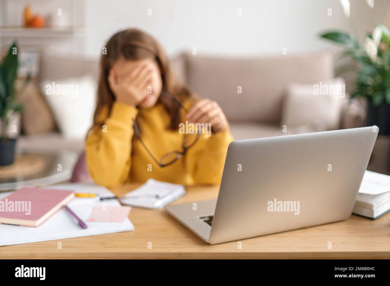 Porträt eines traurigen Mädchens, das müde vom Lernen ist, von zu Hause aus online mit einem Laptop lernt, eine Brille in der Hand hält, erschöpft von Schulaufgaben. Heimunterricht, Fernunterricht durch Covid Stockfoto