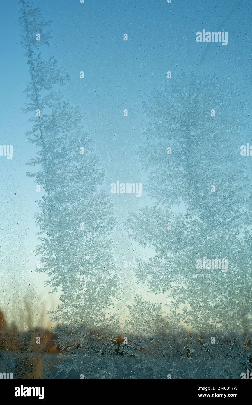 Frostmuster auf der Glasscheibe. Milchglas mit blauem Himmel dahinter. Empfindliche Kristalle, die sich bei kaltem Wetter bilden. Stockfoto