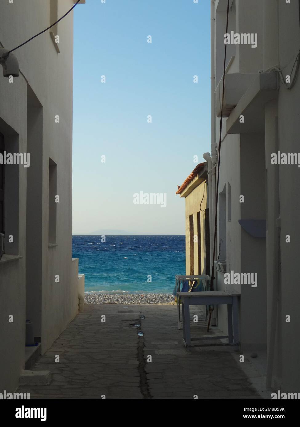 Blick auf das blaue Meer durch eine enge Straße in der Stadt Kokkari. Stockfoto