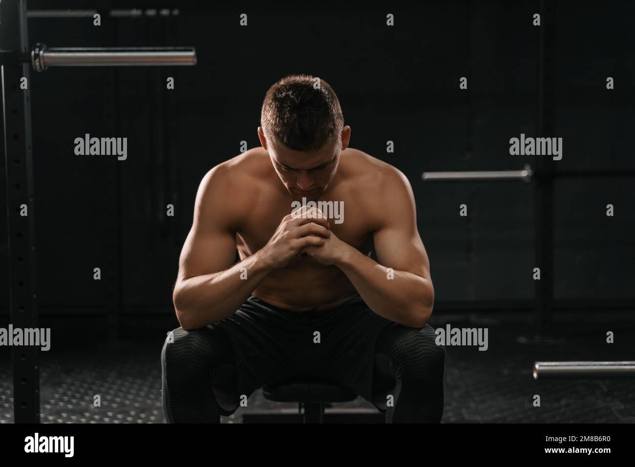 Ein starker, sportlicher Mann, der auf einer Sportbank sitzt und einen Zusammenbruch zu überwinden hat. Demotivationssportkonzept. CrossFit-Training Stockfoto
