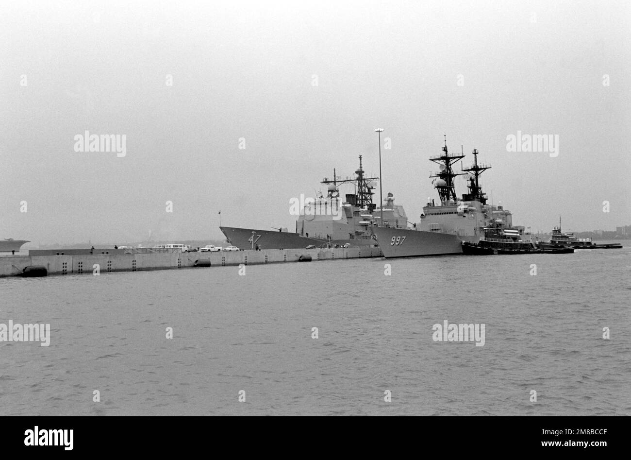 Schleppboote schieben die Zerstörerin USS HAYLER (DD 997) in Richtung ihres Liegeplatzes am Pier 1. Der geführte Raketenkreuzer USS TICONDEROGA (CG 47) liegt auf der anderen Seite des Piers gefesselt. Die TICONDEROGA und DIE HAYLER sind die ersten Schiffe, die am kürzlich fertiggestellten Pier festgemacht wurden. Basis: Marinestützpunkt, New York Bundesstaat: New York (NY) Land: Vereinigte Staaten von Amerika (USA) Stockfoto