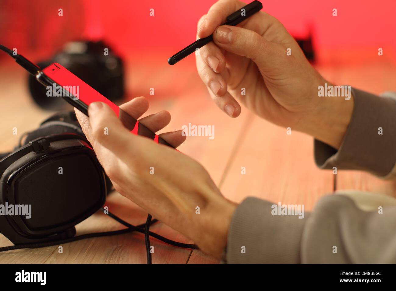 Eine Person schreibt mit einem Eingabestift auf einem Smartphone über Kopfhörer und einen farbigen Hintergrund Stockfoto