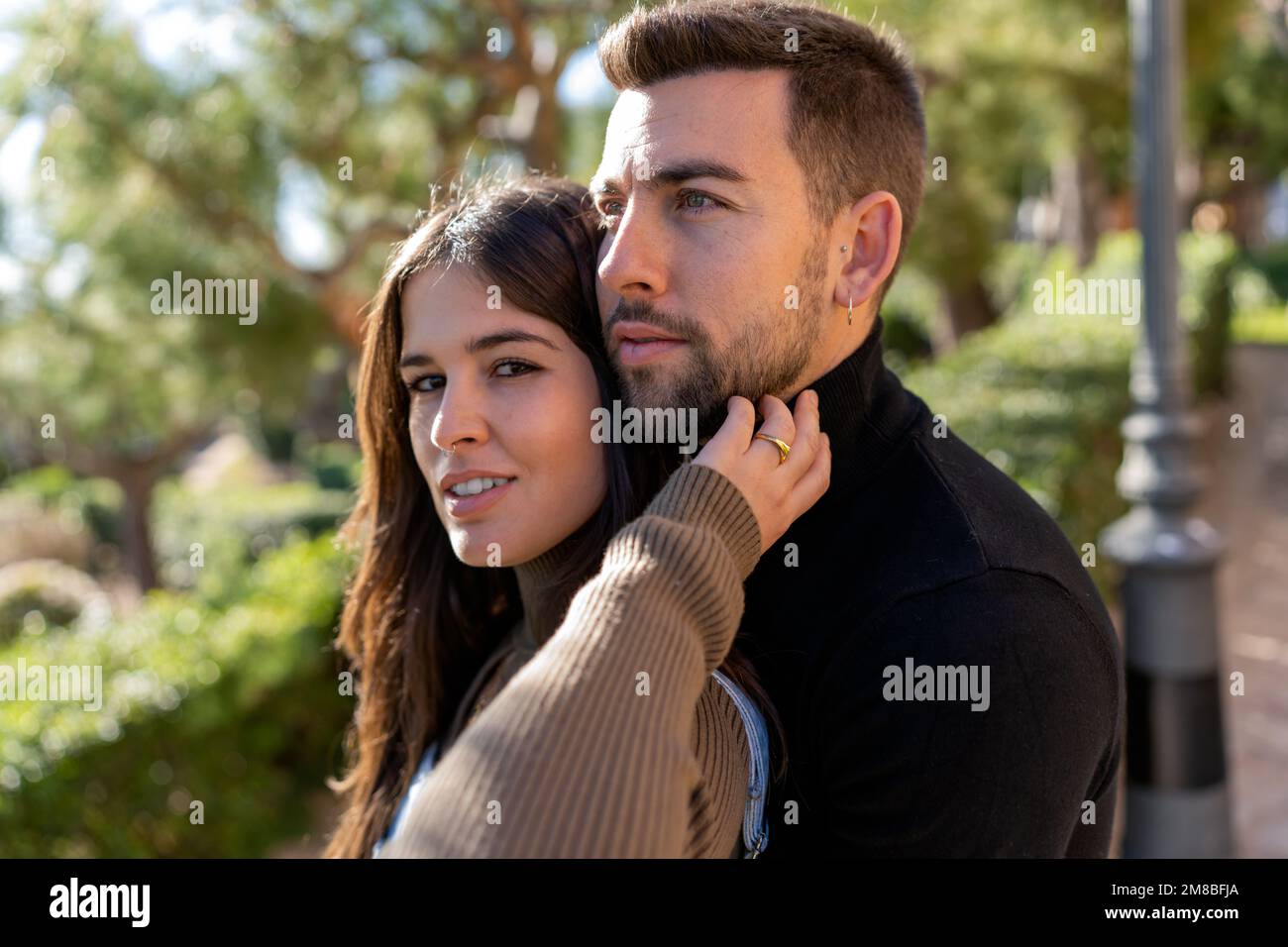 Junge Frau im Pulli berührt Bart des Freundes auf verschwommenem Hintergrund des Parks am Valentinstag Stockfoto