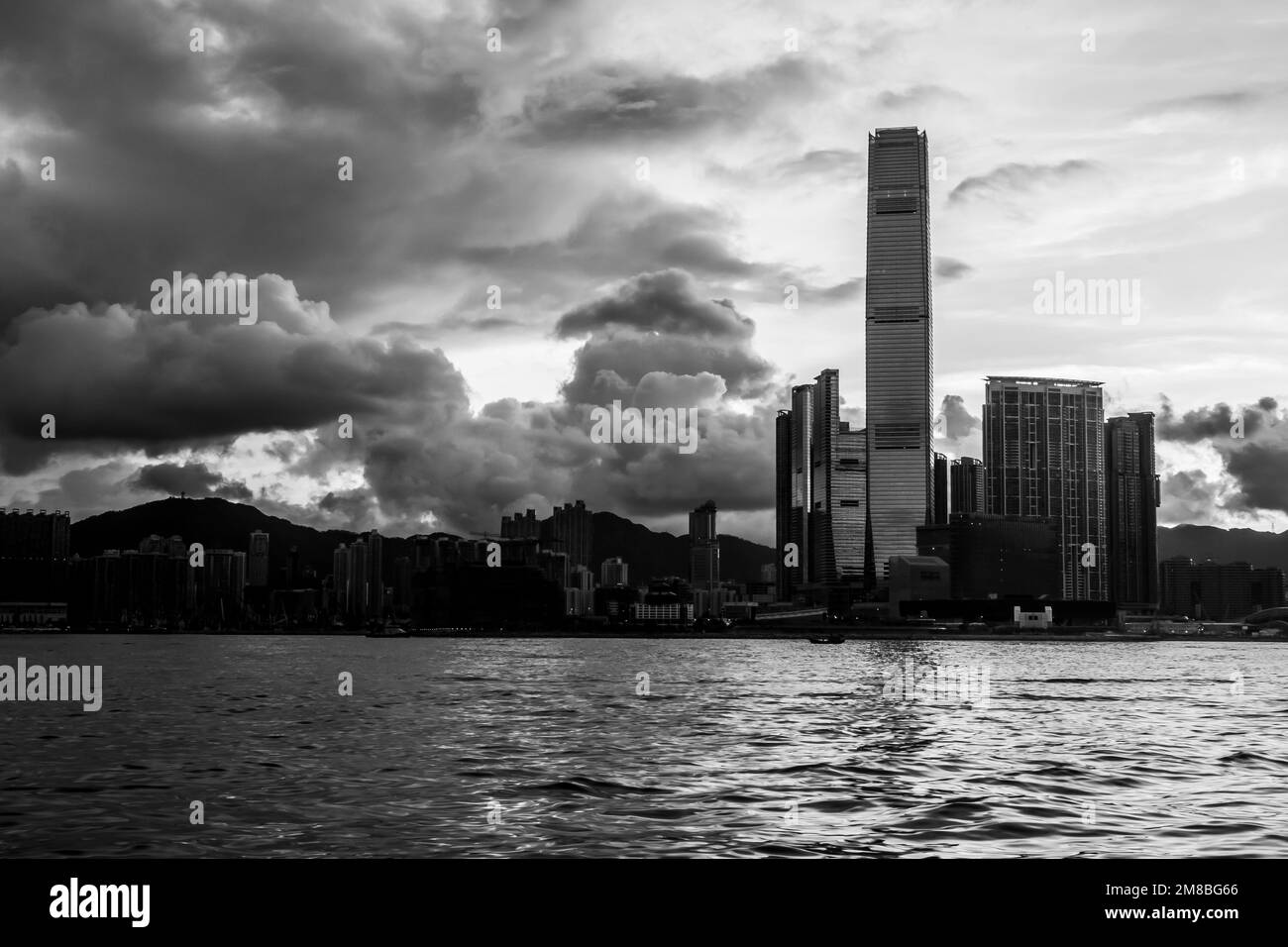 Die Sonne geht über Kowloon in Hongkong auf. Meer im Vordergrund. Gebäude in Silhouette. In Schwarz und Weiß. Stockfoto