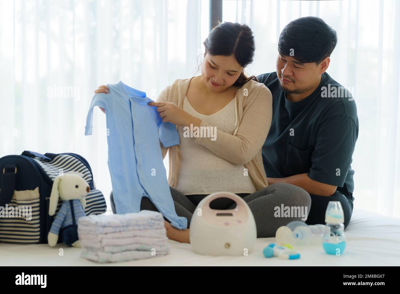 Eine asiatische Schwangere und ihr Mann bereiten Babyphone-Utensilien und Behälter für das Schwangerschaftskonzept zu Hause im Schlafzimmer zu. Stockfoto