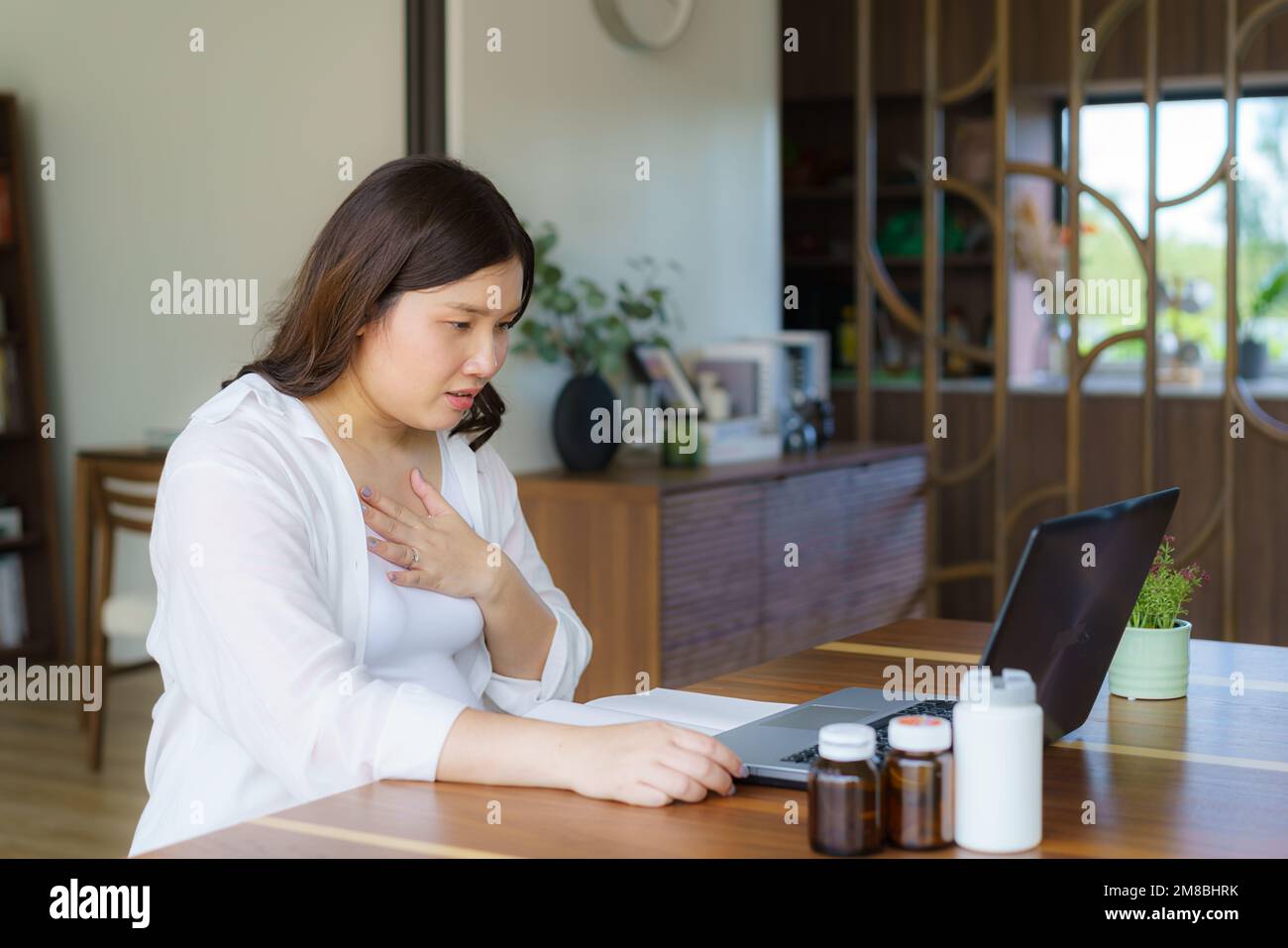 Asiatische Schwangere konsultiert online auf Laptop über ihren Halsschmerzen im Wohnzimmer des Hauses Stockfoto