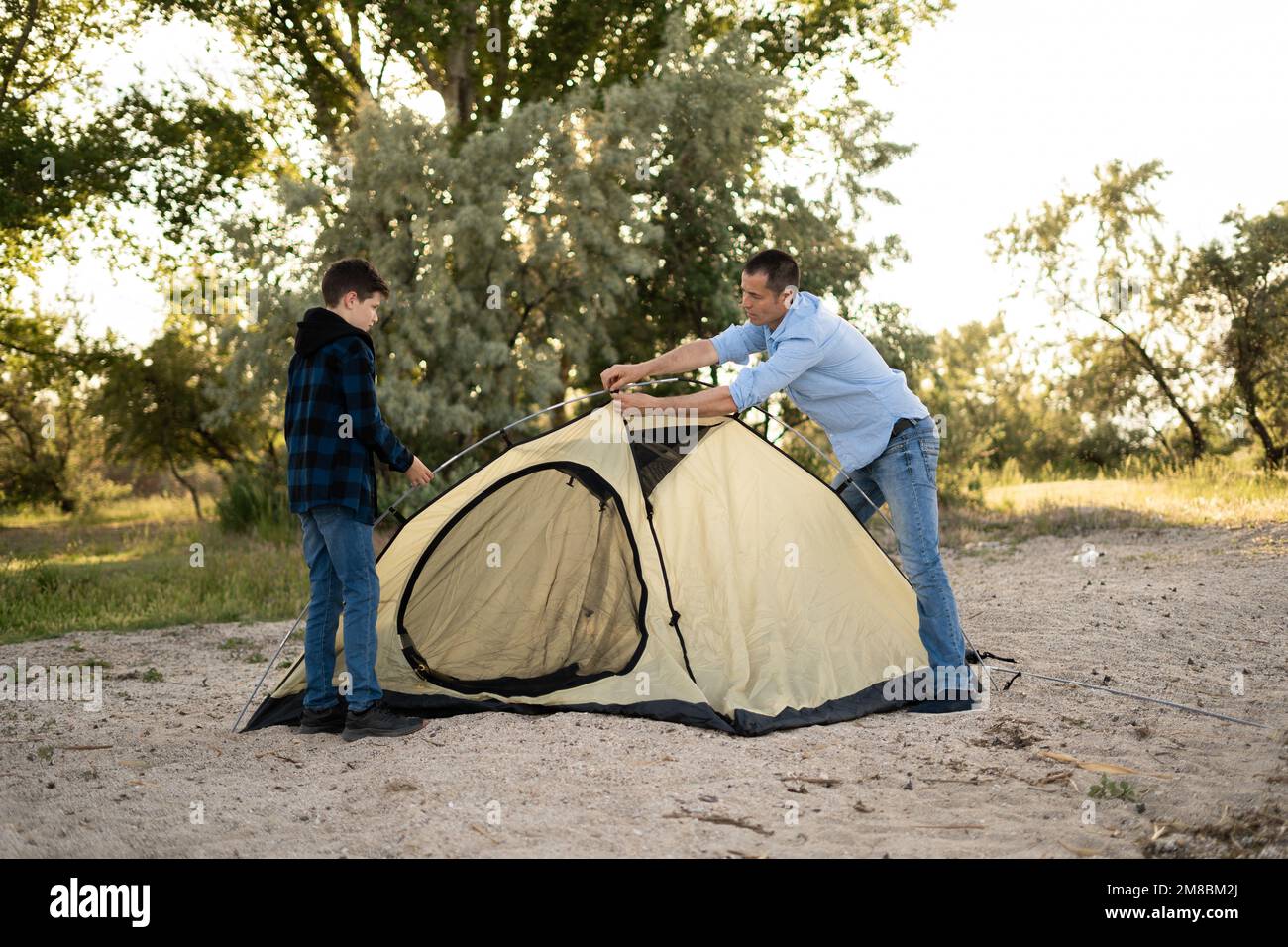 Vater und Sohn installieren Zelt in der Nähe des Flusses. Trekking und Reisen mit Kindern Konzeptbild Stockfoto