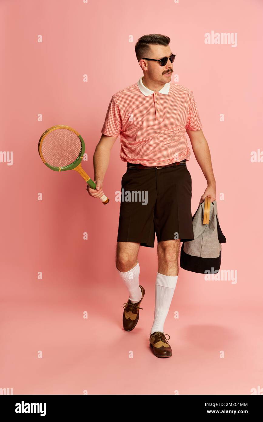 Mitglied des Country Sports Club. Porträts eines gutaussehenden charismatischen Mannes in stilvoller Kleidung, der Tennis im pinkfarbenen Studiohintergrund spielt. Konzept von Stockfoto