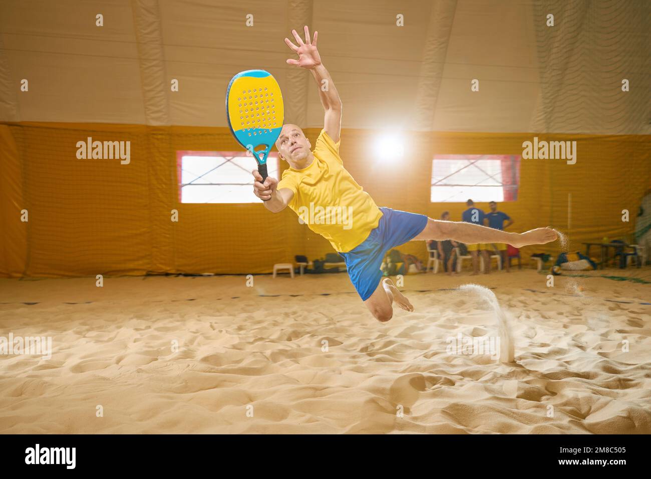 Der Mann fällt mit dem ganzen Körper auf Sand, während er Freskball spielt Stockfoto