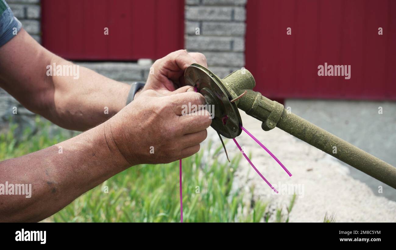 Nahaufnahme einer Hand, die einen Rasenmäher auseinandernimmt, um Teile zu ersetzen. Wartung und Reparatur des Unkrautschneiders durch Austausch von Teilen Stockfoto