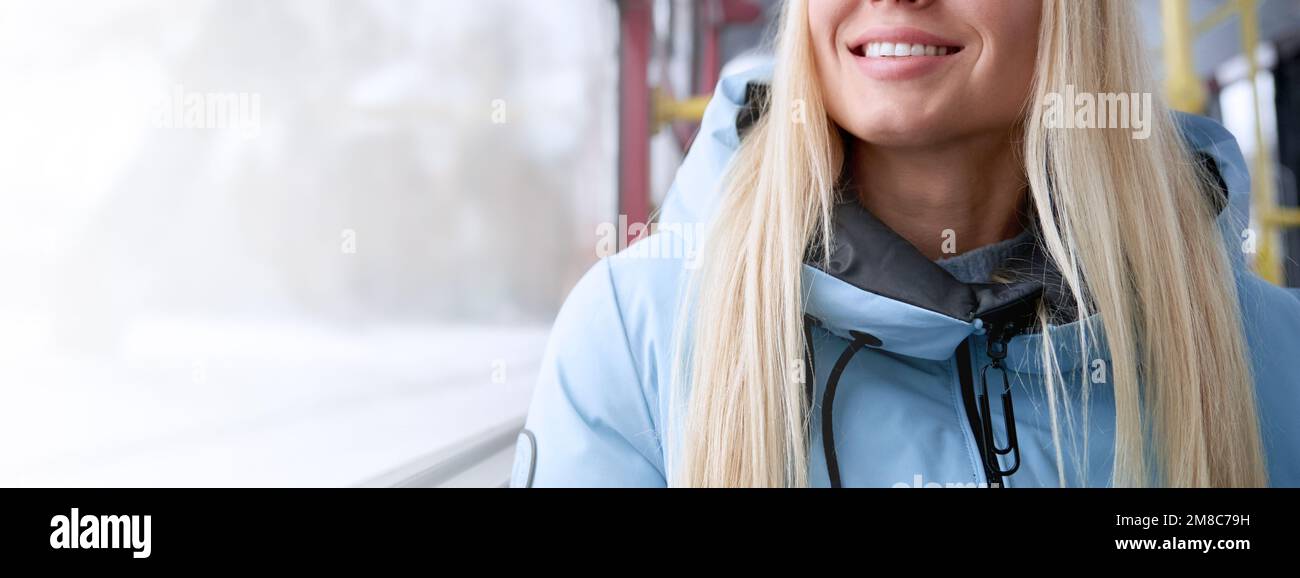 Nahaufnahme einer glücklichen, glücklichen blonden Frau, die mit öffentlichen Verkehrsmitteln unterwegs ist, im Bus sitzt, nach Hause fährt. Attraktive junge Frau, die durch das Fenster schaut. Konzept der täglichen Routine, Stockfoto