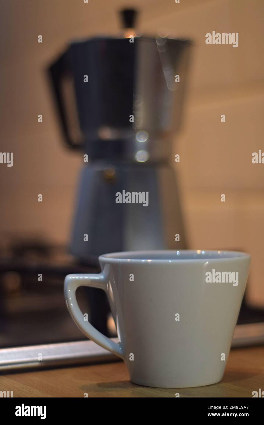 Moka Kanne auf Küchenherd mit Kaffeetasse auf Arbeitsplatte Stockfoto
