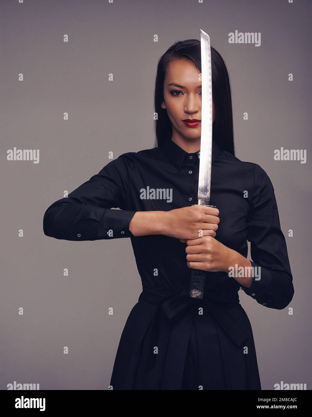 Porträt, Samurai und Krieger mit einer asiatischen Frau im Studio auf grauem Hintergrund für Kampfsport oder Kampf. Training, Fantasie und Waffe mit einem Modell Stockfoto