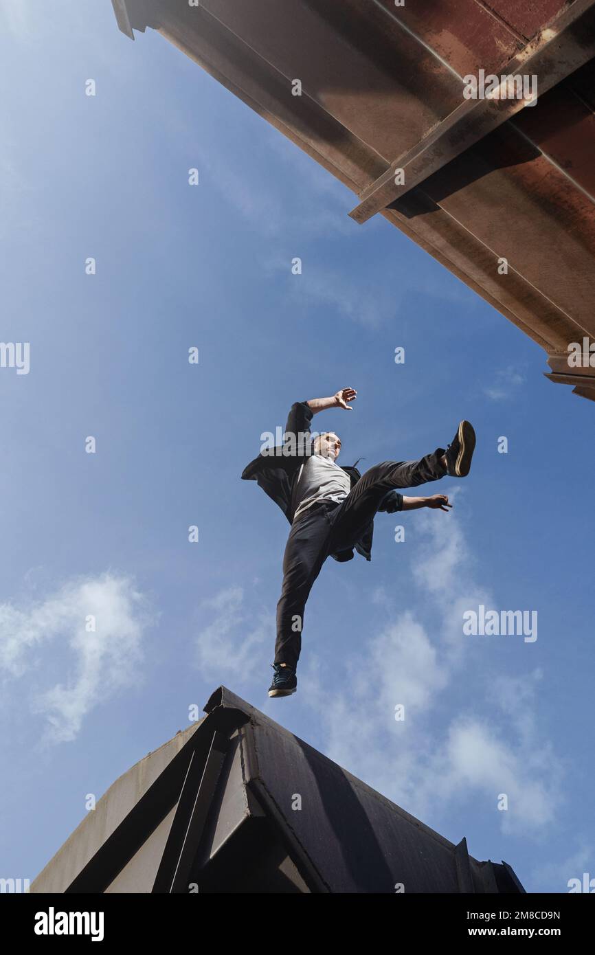 Ein Mann, der gruselig zwischen den Dächern springt. Ein Typ, der Parkour-Freerunning praktiziert. Stockfoto