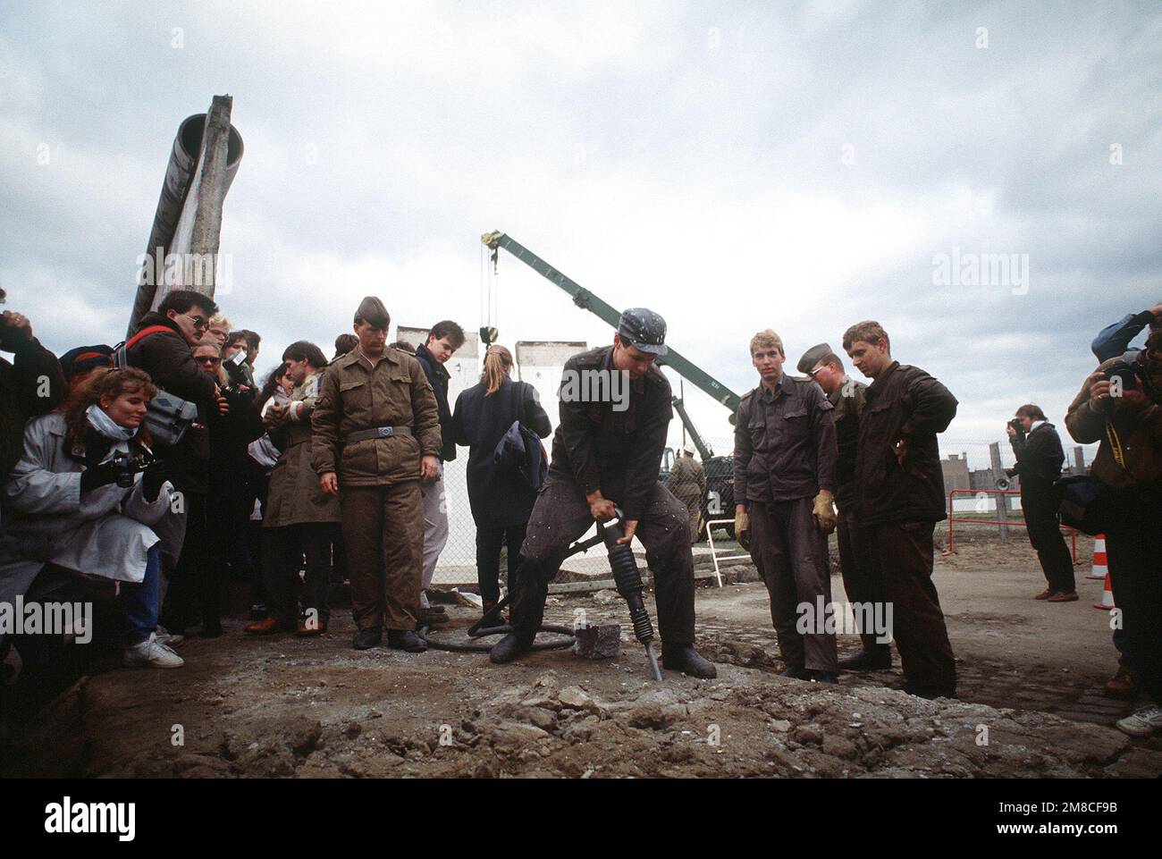 Die ostdeutsche Polizei und westdeutsche Bürger beobachten, wie ein Arbeiter einen Abschnitt der Berliner Mauer am Potsdamer Platz abbaut. Basis: Berlin Land: Deutschland / Deutschland (DEU) Stockfoto