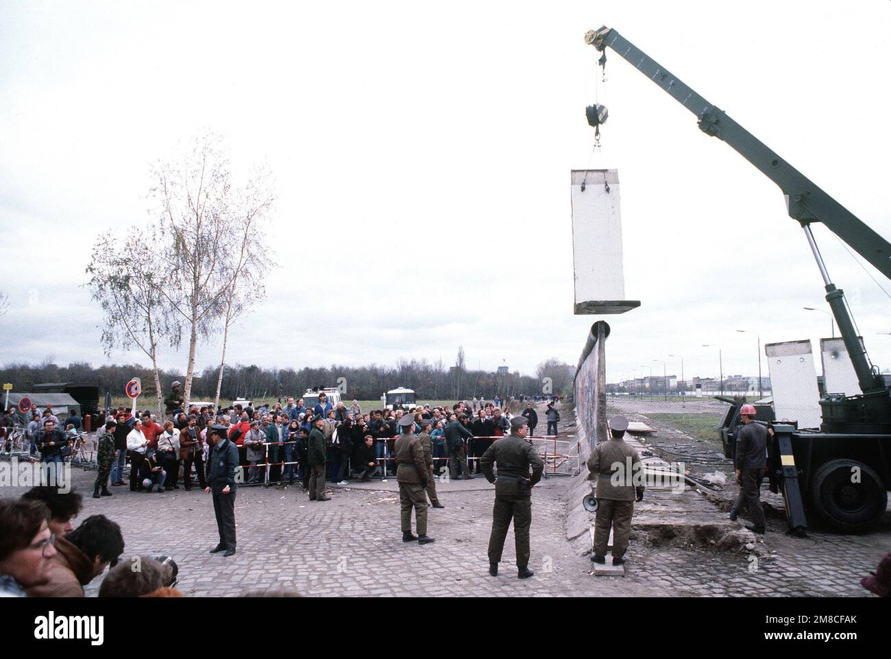 Die ostdeutsche Polizei und westdeutsche Bürger beobachten, wie ein Arbeiter einen Abschnitt der Berliner Mauer am Potsdamer Platz abbaut. Basis: Berlin Land: Deutschland / Deutschland (DEU) Stockfoto
