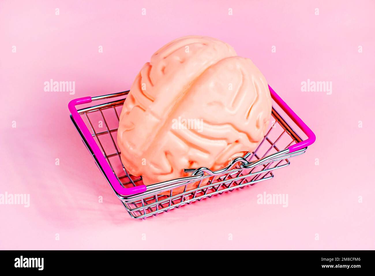 Leuchtend pinkfarbenes menschliches Gehirn im Metalleinkaufskorb auf magentafarbenem Hintergrund. Bildung, intelligenter Einkauf, kommerzielles Kreativitätskonzept. Stockfoto
