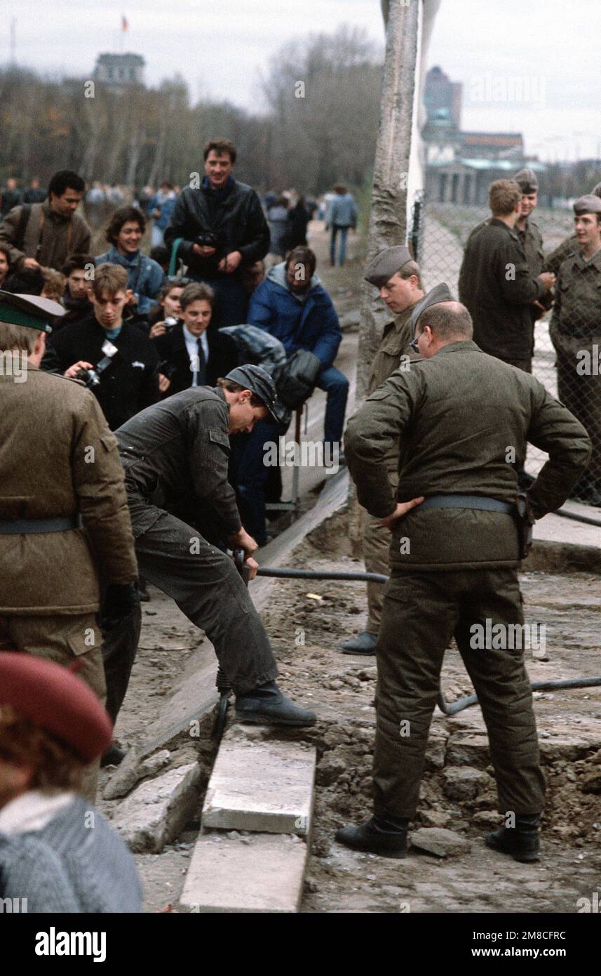 Die ostdeutsche Polizei und westdeutsche Bürger beobachten, wie ein Arbeiter einen Abschnitt der Berliner Mauer am Potsdamer Platz abbaut. Basis: Berlin Land: Deutschland / Deutschland (DEU) Stockfoto