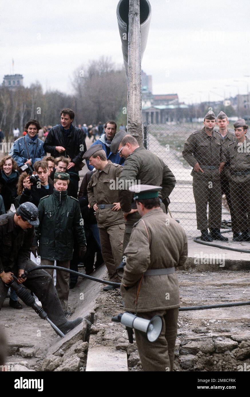 Die ostdeutsche Polizei und westdeutsche Bürger beobachten, wie ein Arbeiter einen Abschnitt der Berliner Mauer am Potsdamer Platz abbaut. Basis: Berlin Land: Deutschland / Deutschland (DEU) Stockfoto