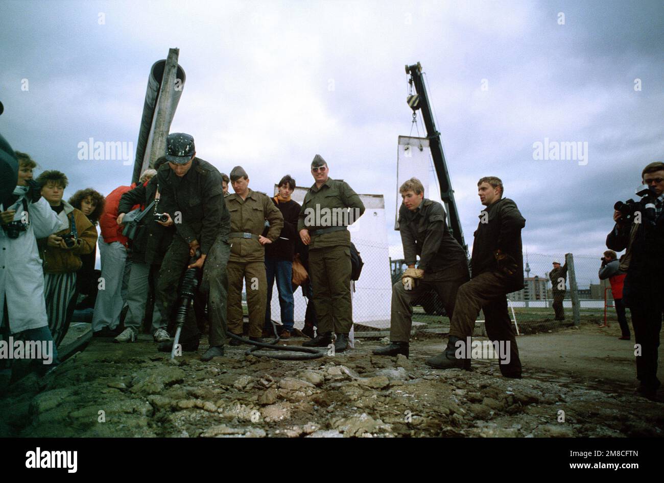 Die ostdeutsche Polizei und westdeutsche Bürger beobachten, wie ein Arbeiter einen Abschnitt der Berliner Mauer am Potsdamer Platz abbaut. Basis: Berlin Land: Deutschland / Deutschland (DEU) Stockfoto