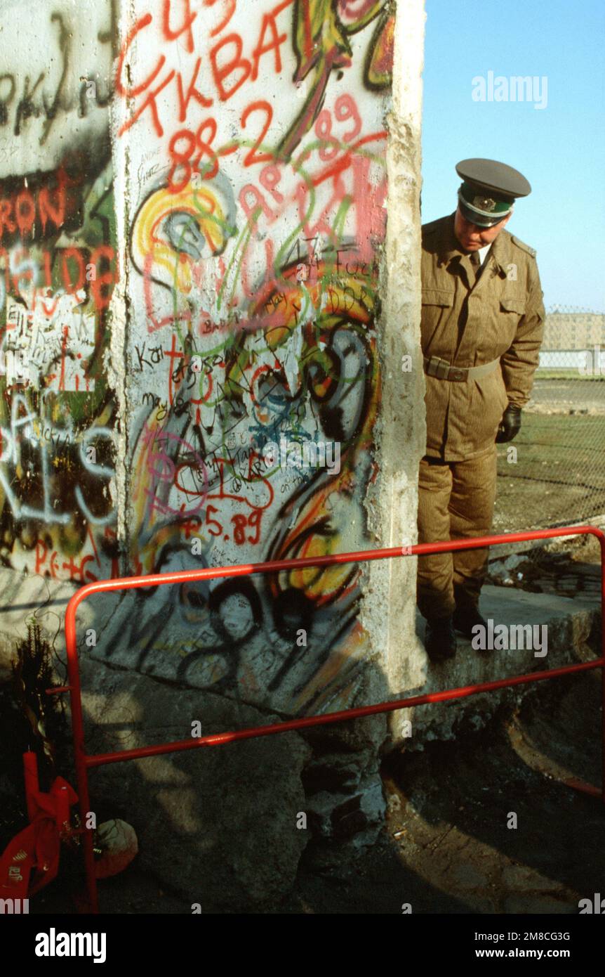 Ein ostdeutscher Polizist schaut auf einen kleinen Weihnachtsbaum, der die westdeutsche Seite der Berliner Mauer schmückt. Die Wache steht an der neu geschaffenen Öffnung der Berliner Mauer am Potsdamer Platz. Basis: Berlin Land: Deutschland / Deutschland (DEU) Stockfoto