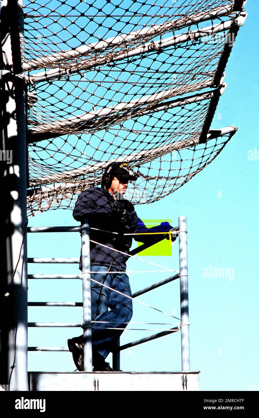 Ein Besatzungsmitglied an Bord des amphibischen Angriffsschiffs USS WASP (LHD 1) beobachtet die Andockmanöver, während das Schiff in den Hafen einläuft. Das Crewmitglied trägt schallbetriebene Telefone. Basis: Marine Air Station, Norfolk Bundesstaat: Virginia (VA) Land: Vereinigte Staaten von Amerika (USA) Stockfoto