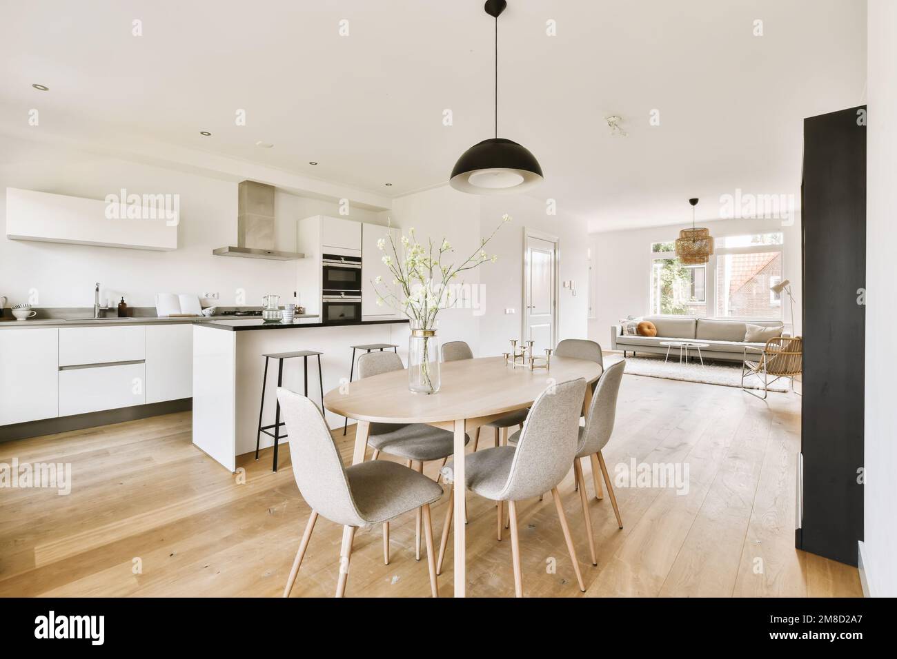 Küche, Esszimmer und Wohnbereich in einem Apartment mit weißen Wänden und Holzfußboden der Tisch ist von grauen Stühlen umgeben Stockfoto