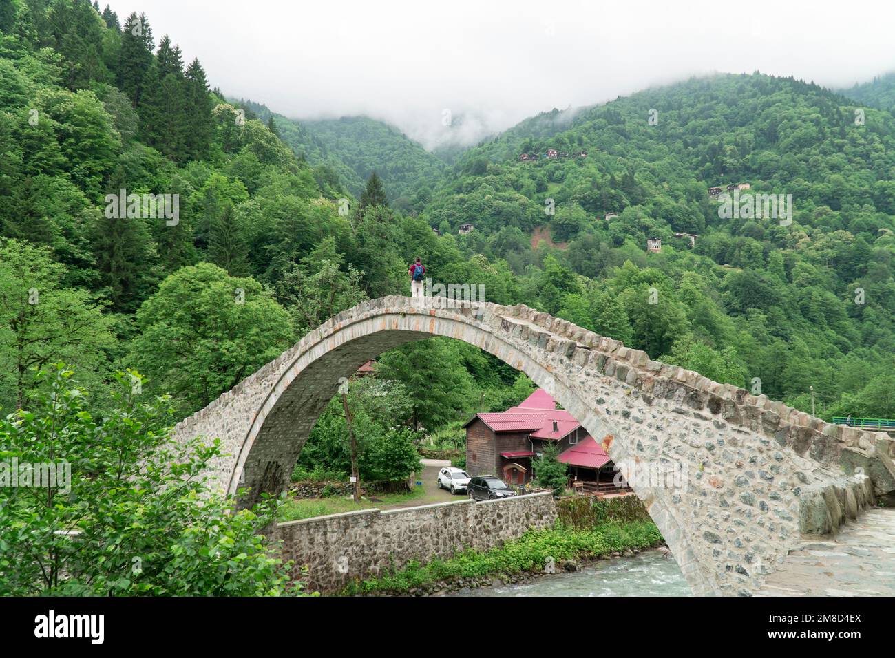 Alte Fußgängerbrücke aus Stein. Tourist steht auf der Brücke Senyuva über den Firtina Fluss in Camlihemsin, Rize, Türkei Stockfoto