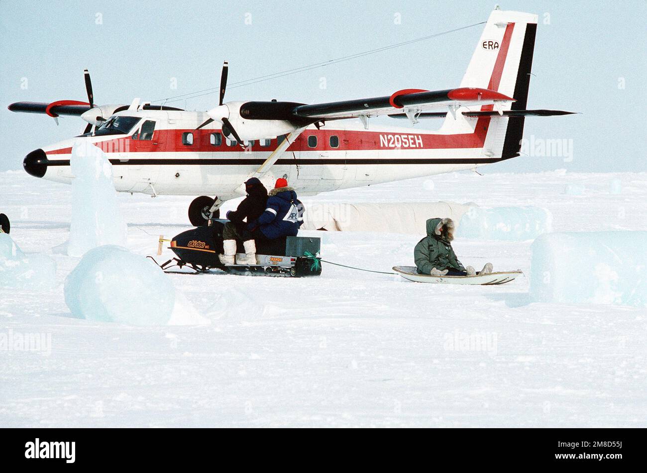Wissenschaftler am Ice Camp Aplis nutzen ein Schneemobil für den Transport. Ein kommerzielles DHC-3 Otter-Flugzeug parkt am Camp. Land: Nordsee Stockfoto
