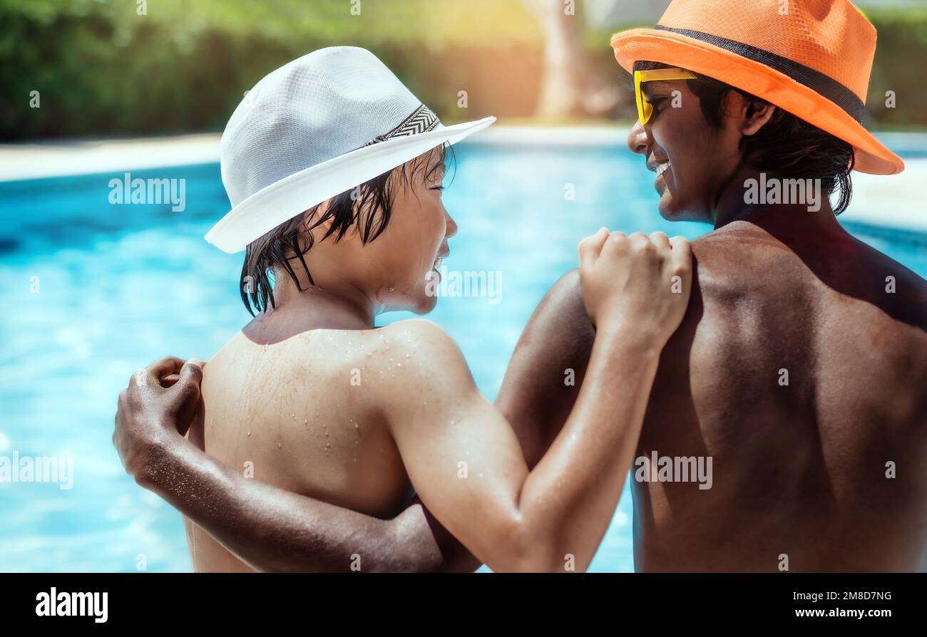 Nahaufnahme von zwei Freunden indischer und chinesischer Herkunft, die Hüte und Gläser trugen und sich am Pool freudig umarmten. Urlaubskonzept, Stockfoto