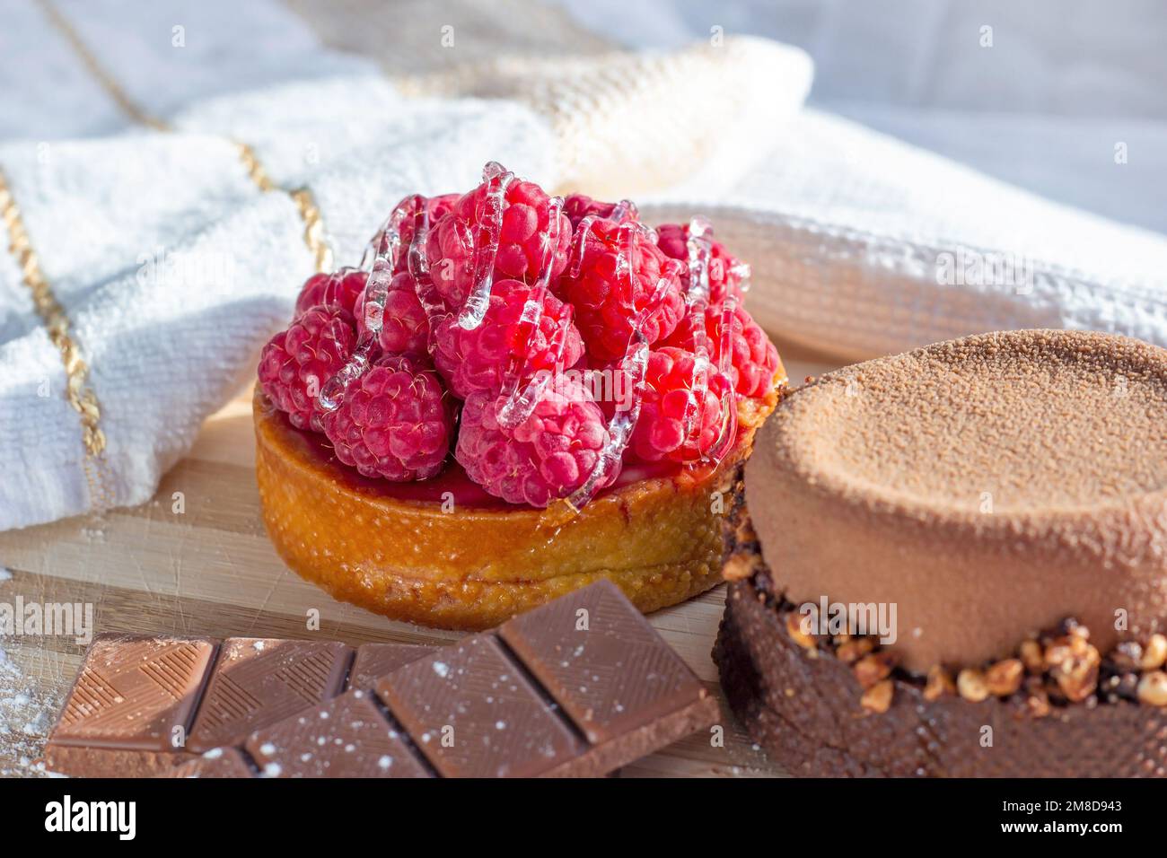 Frische Himbeeren- und Schokoladentörtchen auf dem Küchentisch im Hintergrund. Stockfoto