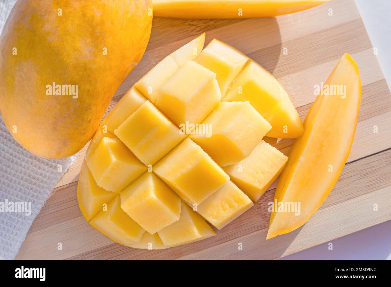 Draufsicht auf leuchtend gelbes Würfel, frische Mango auf Holzschneidbrett, Nahaufnahme. Stockfoto
