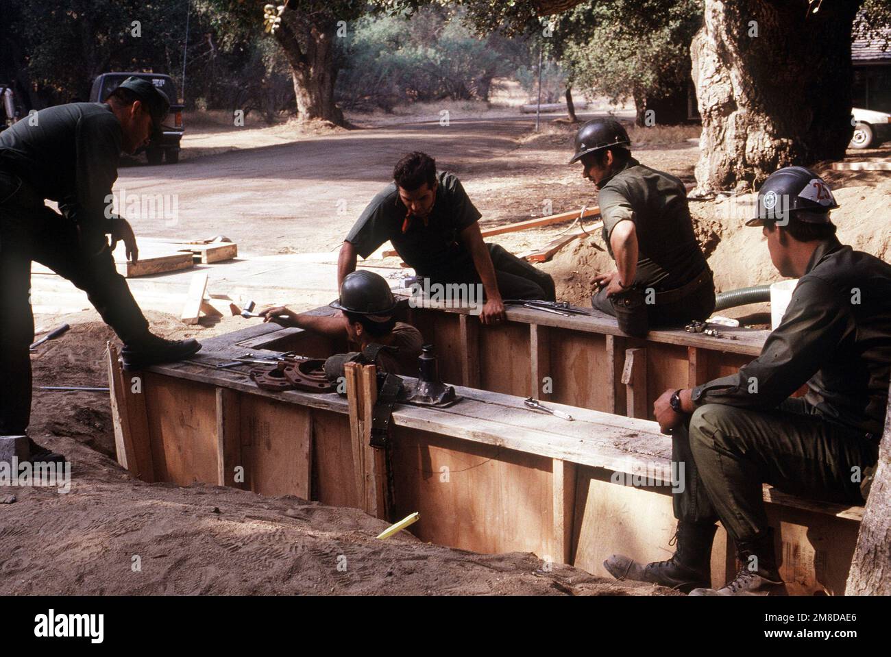 Vier Mitglieder eines mobilen Baubataillons der Navy beobachten einen anderen Seabee, der in einer Betonform arbeitet, während er ein neues Wassersystem im Mataguay Boy Scout Reservation installiert. Das Wassersystem ist Teil einer umfassenden Überholung des Lagers durch verschiedene Einheiten der Reserve Naval Construction Force. Basis: Santa Ysabel Staat: Kalifornien (CA) Land: Vereinigte Staaten von Amerika (USA) Stockfoto
