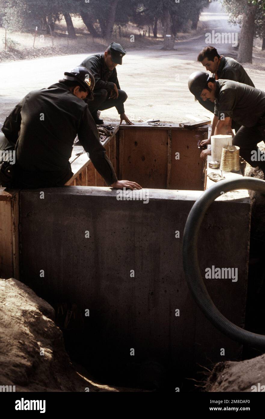 Vier Mitglieder eines mobilen Baubataillons der Navy beobachten einen anderen Seabee, der in einer Betonform arbeitet, während er ein neues Wassersystem im Mataguay Boy Scout Reservation installiert. Das Wassersystem ist Teil einer umfassenden Überholung des Lagers durch verschiedene Einheiten der Reserve Naval Construction Force. Basis: Santa Ysabel Staat: Kalifornien (CA) Land: Vereinigte Staaten von Amerika (USA) Stockfoto