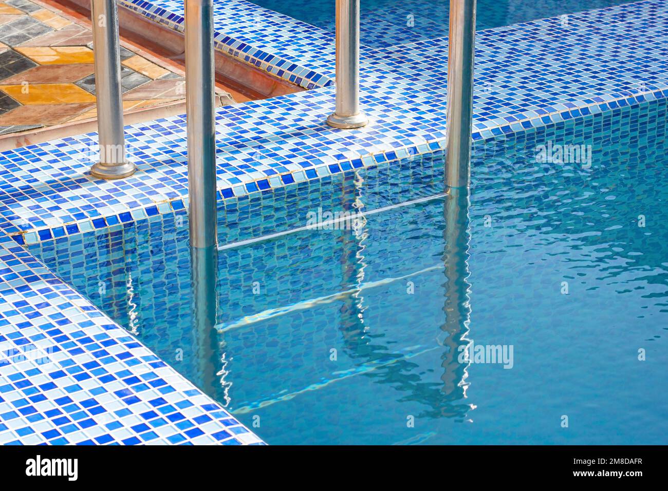 Eine Metall Swimming Pool Safe Leiter (Skimmer) am Eingang zum Haus auf der Poolseite mit dem blauen sauberen Wasser. Stockfoto