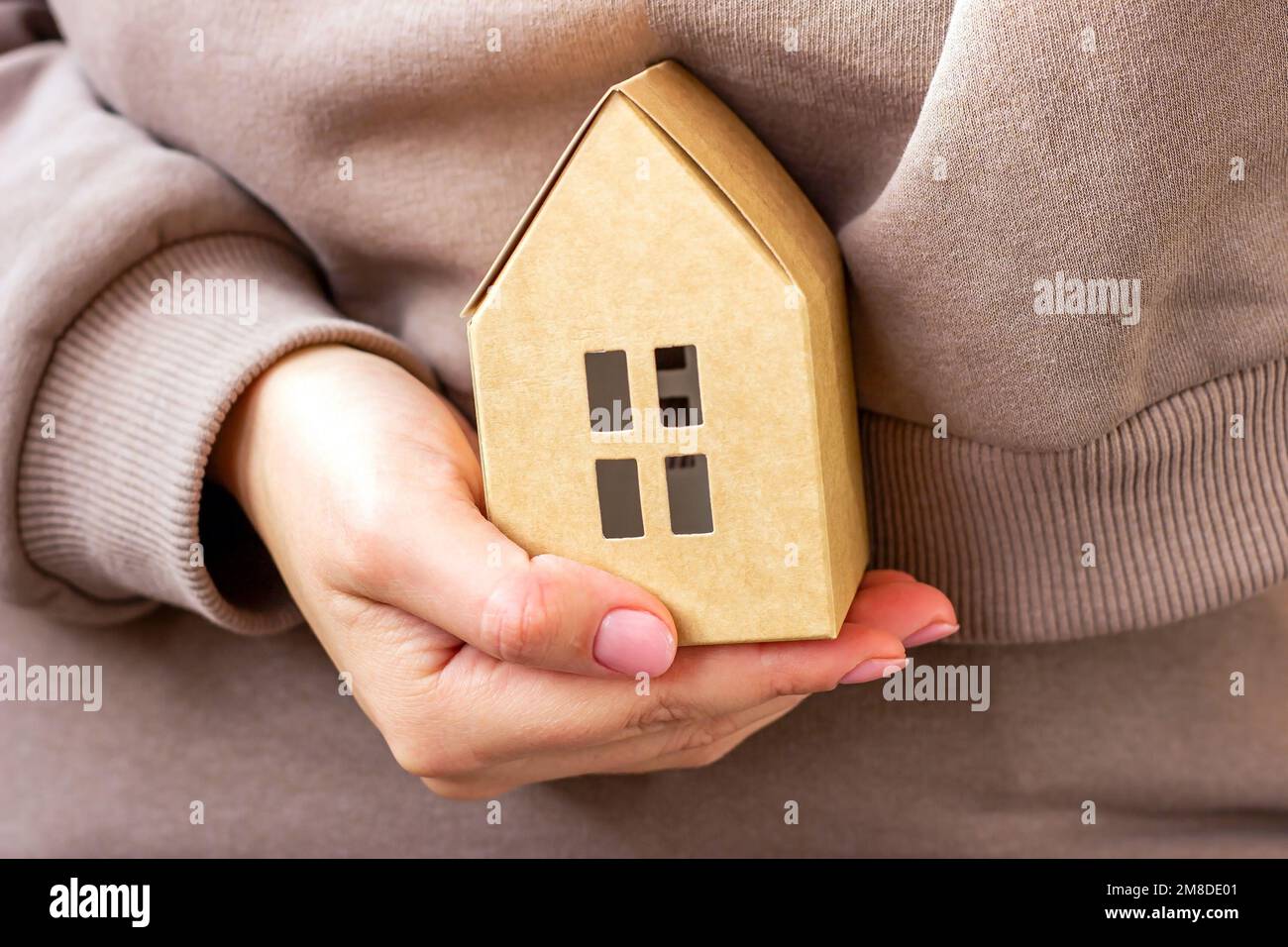 Ein kleines Papierhaus in der Hand einer Frau aus der Nähe. Immobilien- und Sachversicherungs-Konzept. Stockfoto