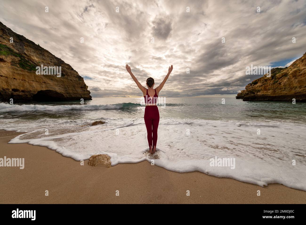 Sportliche Frau, die im Meer steht, mit erhobenen Armen, um dem Alltag zu entfliehen. Stockfoto